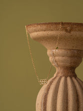 The CAMELLIA 555 Angel Number Choker with Peridot is displayed draped over a textured beige ceramic vase, set against an olive green backdrop.